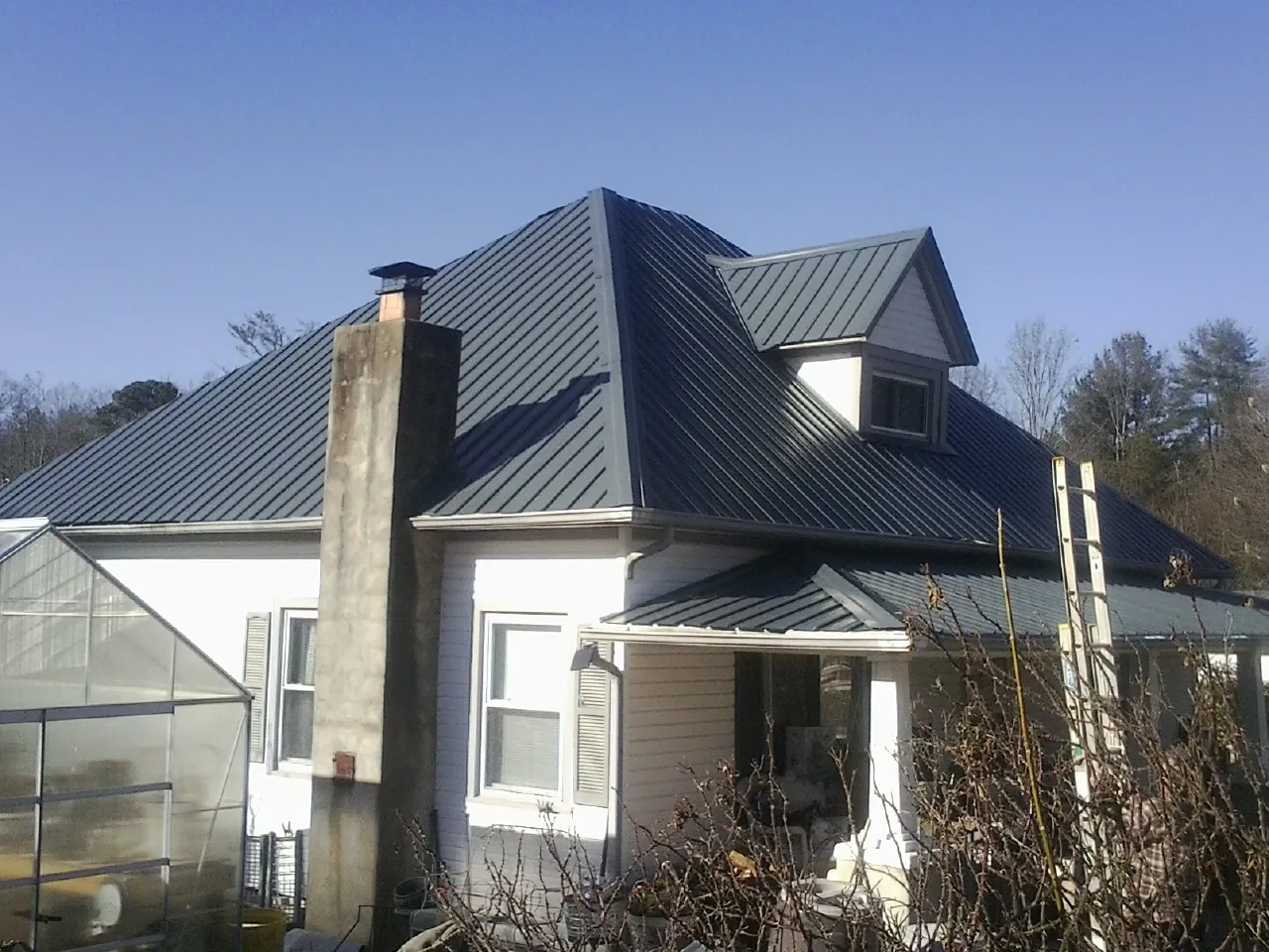 Dark blue standing seam metal roof on a white farmhouse with dormer — Slate & Tile Roof Repair by Roofing Brothers in Johnsonburg