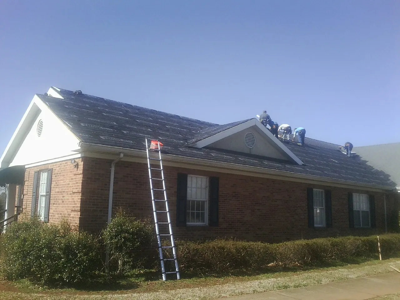 Crew tearing shingles off a brick ranch roof with a ladder set — Metal Roof Repair work by our crew in Johnsonburg