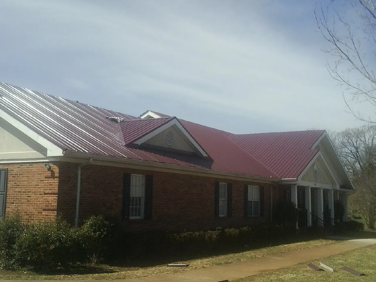 Red metal roof with gabled entries on a long brick building, from a Hail Damage Roof Repair job in Johnsonburg