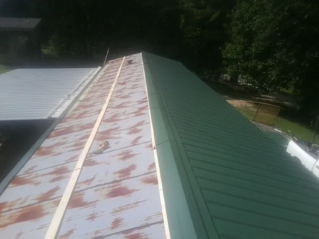 Old rusted panels beside newly installed green metal roofing — Wind Damage Roof Repair by Roofing Brothers in Johnsonburg