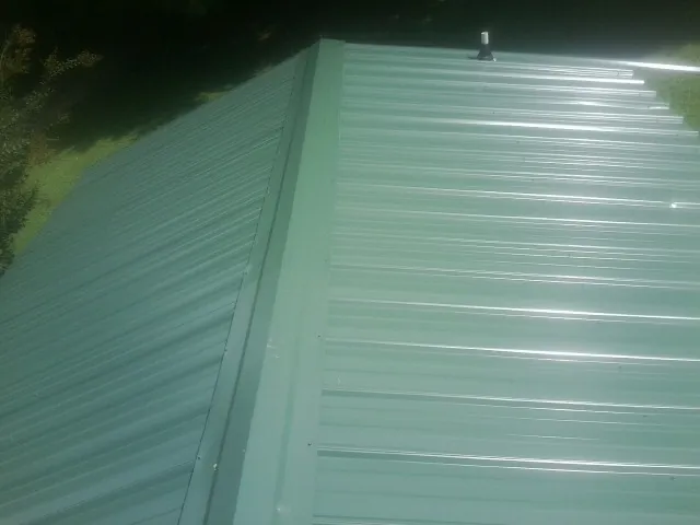 New green metal panels meeting at the ridge of a roof — Flat Roof Repair work by our crew in Johnsonburg