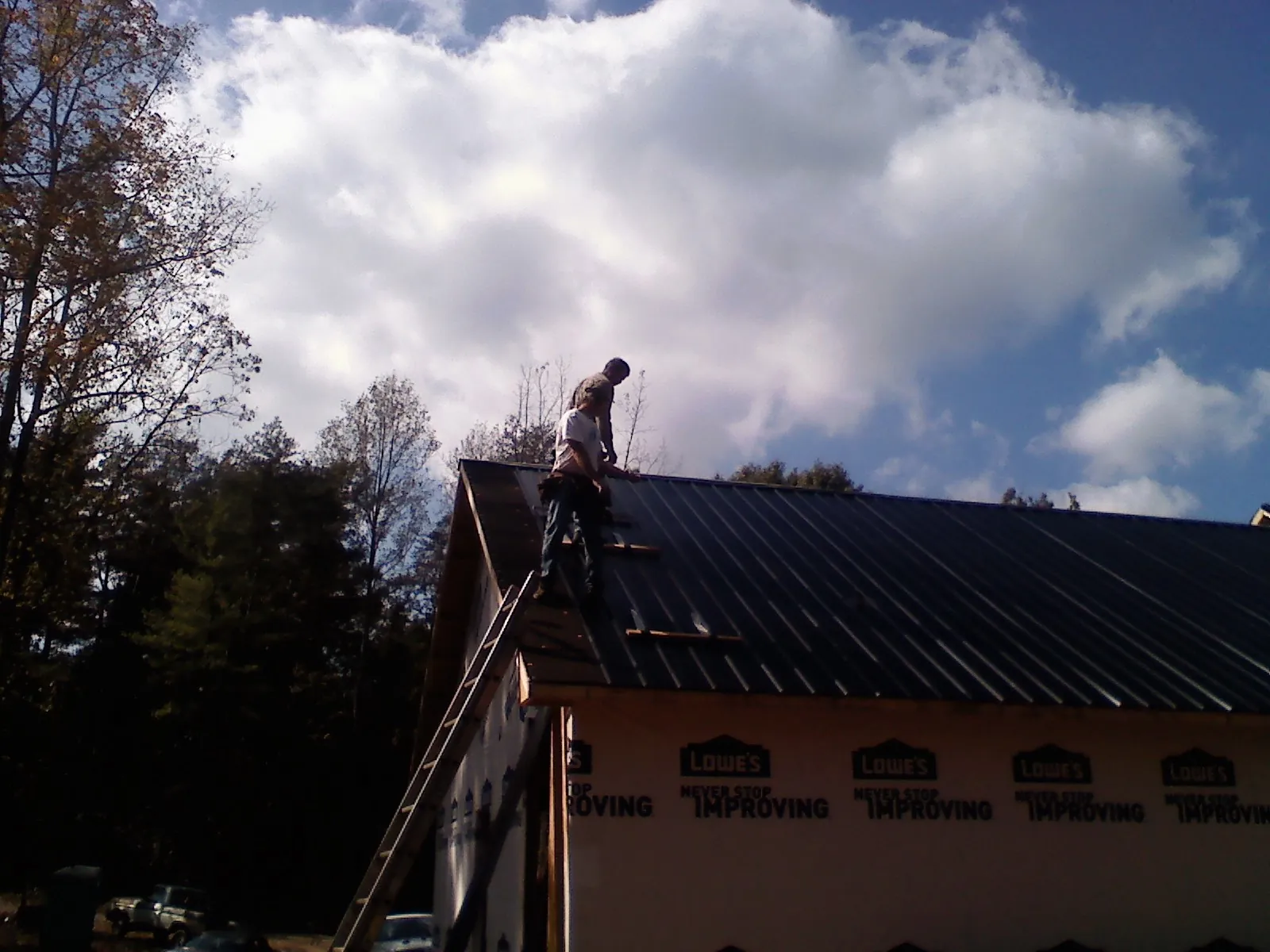 Roofer fastening dark metal panels high against a cloudy sky, from a Roof Inspection job in Johnsonburg