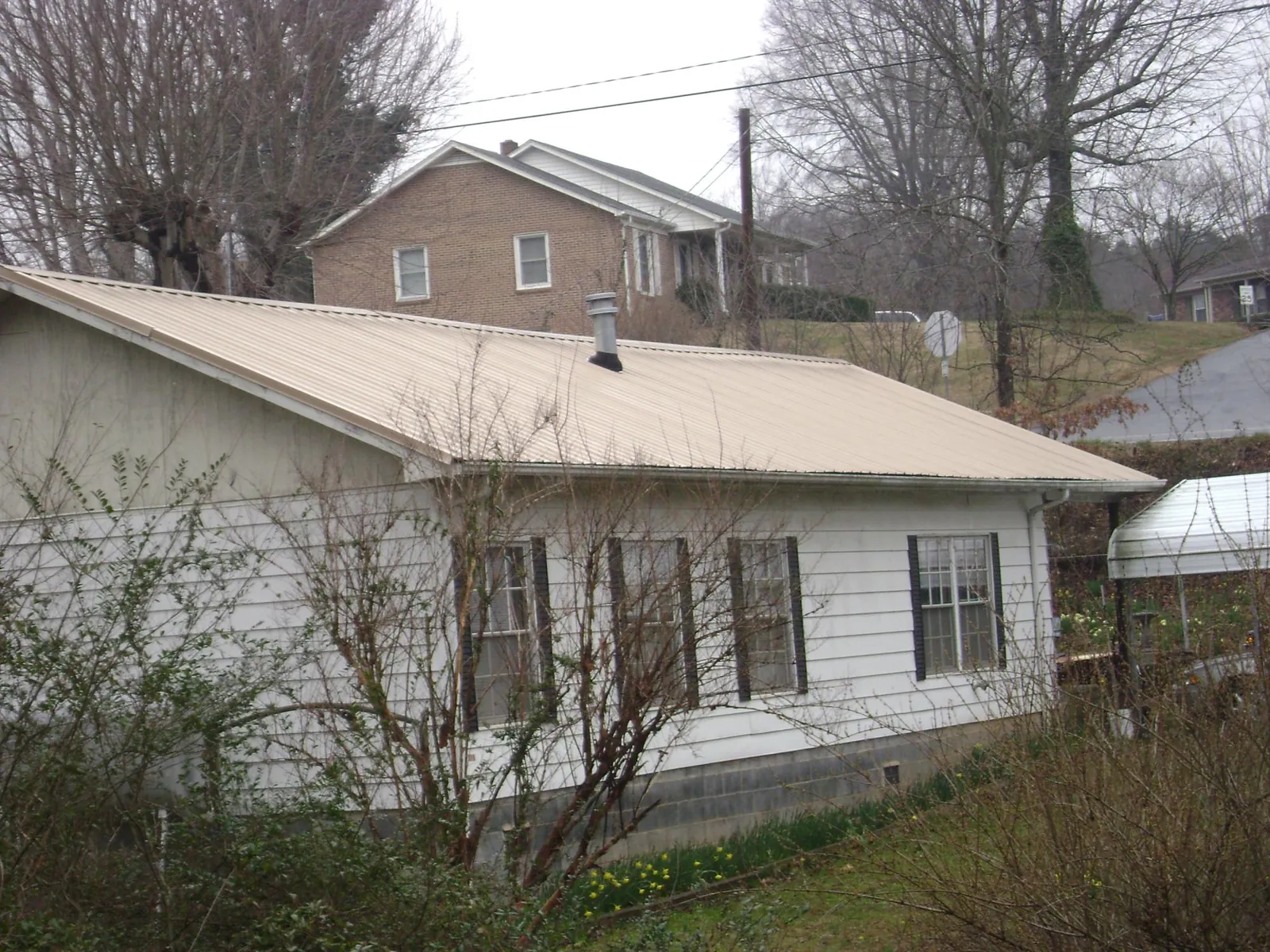 Tan metal roof on a white sided house set into a hillside — Commercial Roofing by Roofing Brothers in Johnsonburg